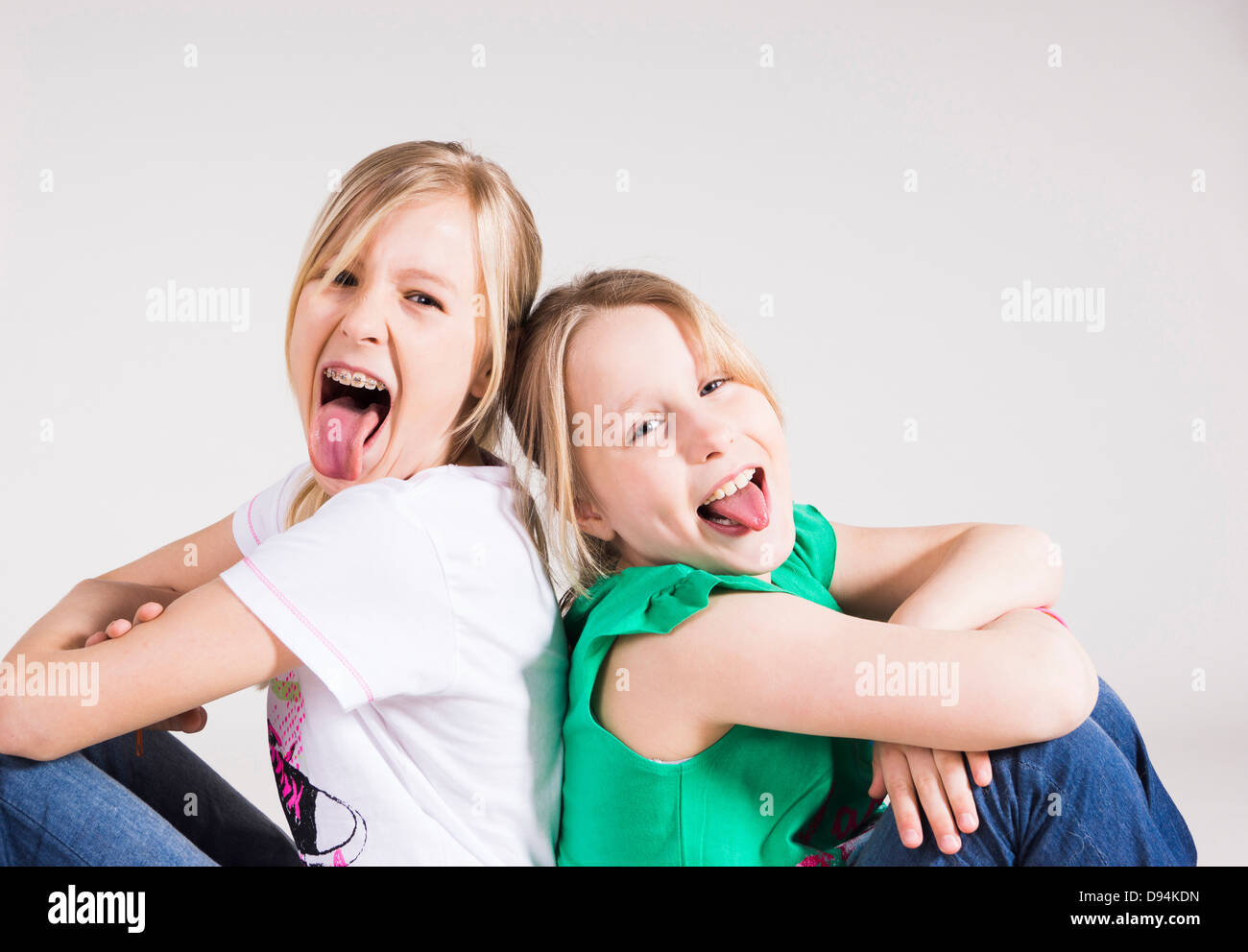 Portrait of Girls Sitting Back to Back and Sticking their Tongues Out Stock Photo