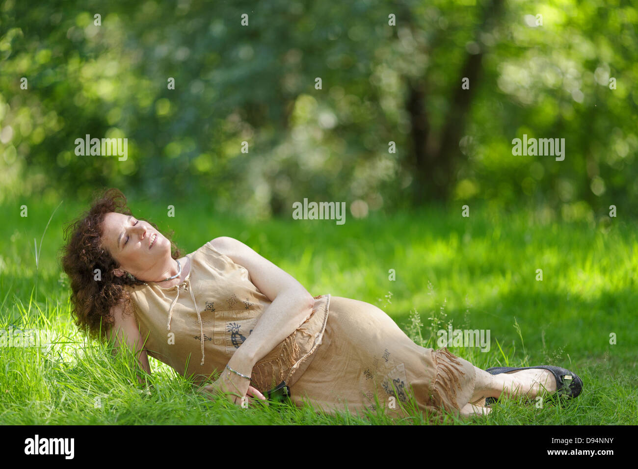 Middle aged mature woman lying in fresh spring grass under sunlight Stock Photo