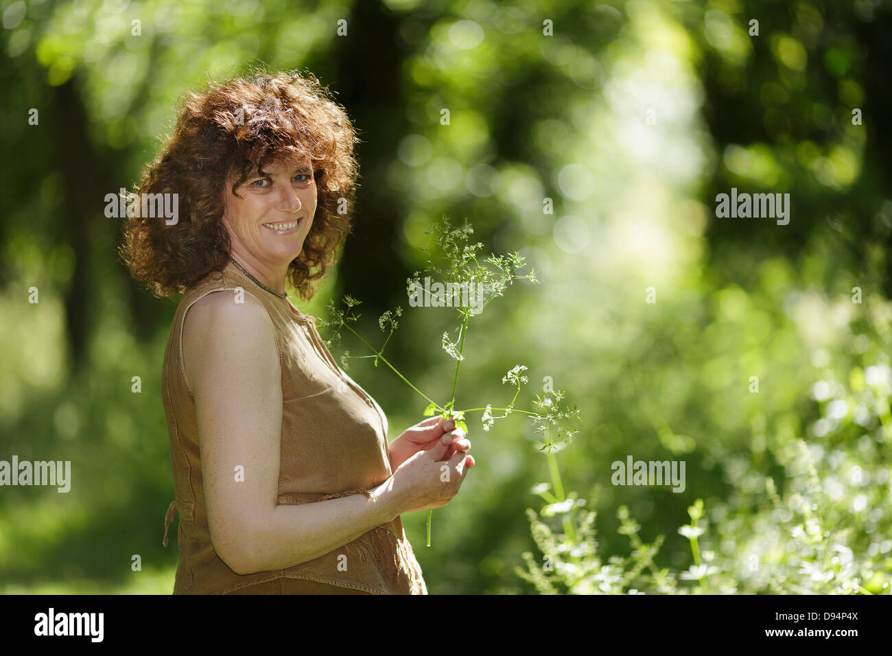 Middle aged mature woman enjoying nature holding wildflower in forest Stock Photo