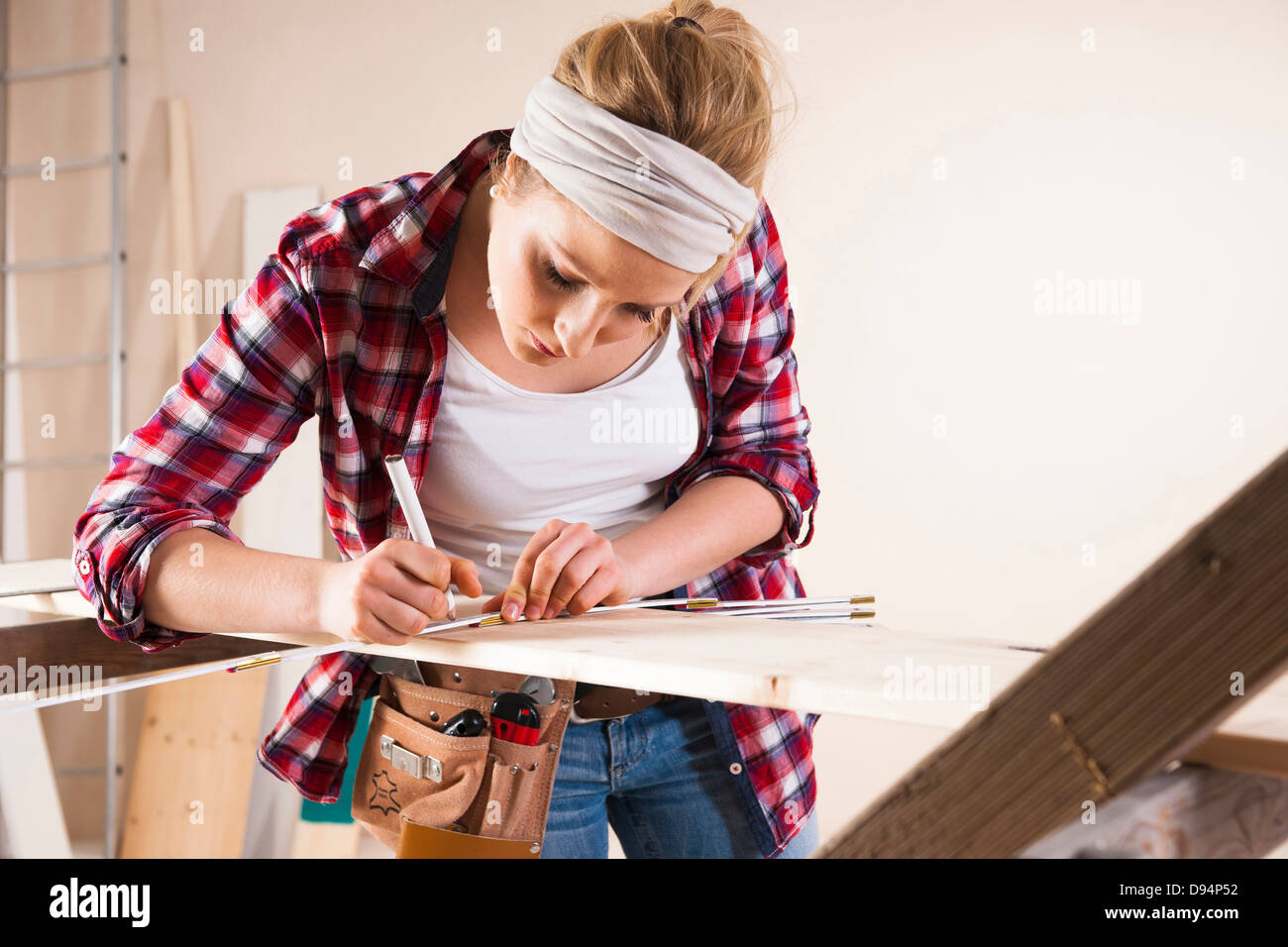 Studio Shot of Young Woman Measuring Lumber Stock Photo