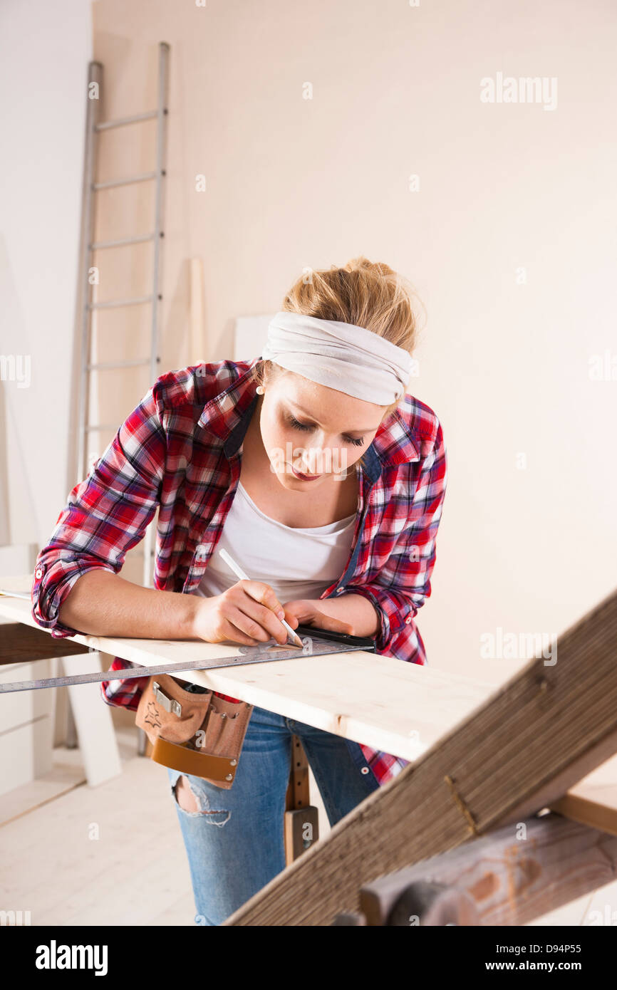 Studio Shot of Young Woman Measuring Lumber Stock Photo