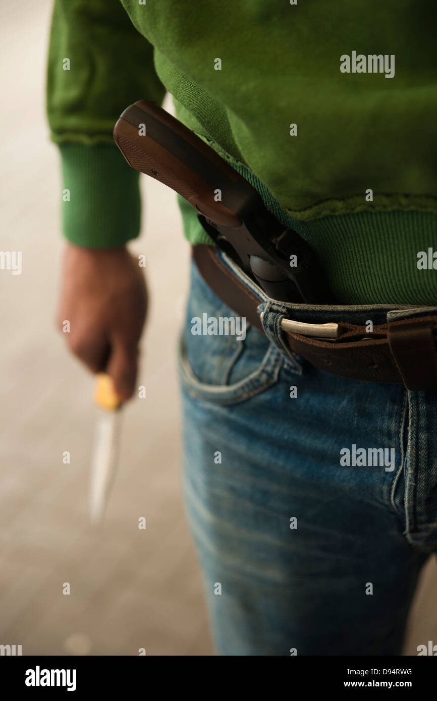 Close-up of Young Man holding Knife with Handgun tucked into Waistband of Blue Jeans, Mannheim. Baden-Wurttemberg, Germany Stock Photo