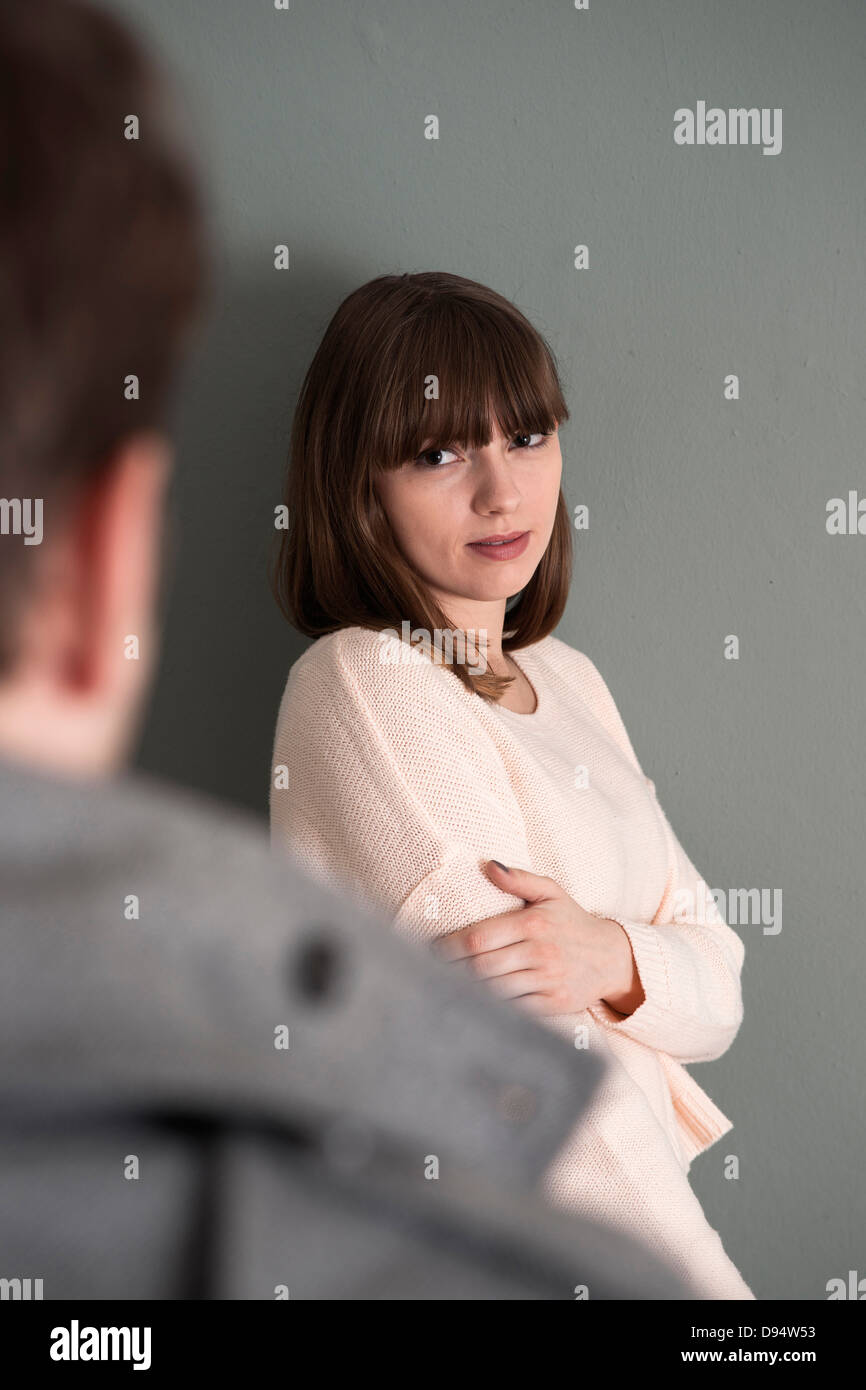 Portrait of Young Woman Standing in front of Young Man, Looking at him Intensely, Studio Shot on Grey Background Stock Photo