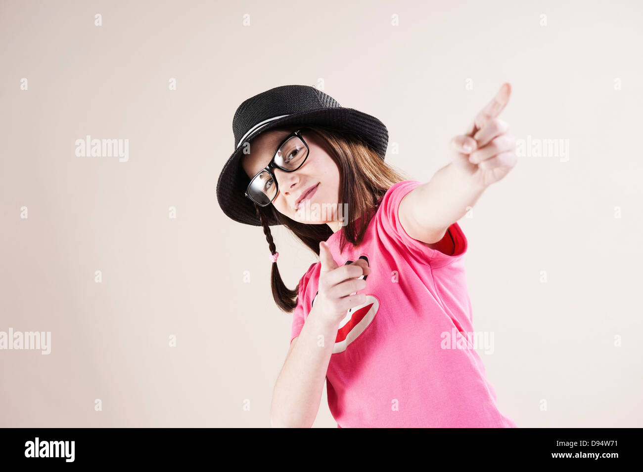 Portrait of Girl wearing Fedora and Horn-rimmed Eyeglasses, Pointing and Smiling at Camera, Studio Shot on White Background Stock Photo