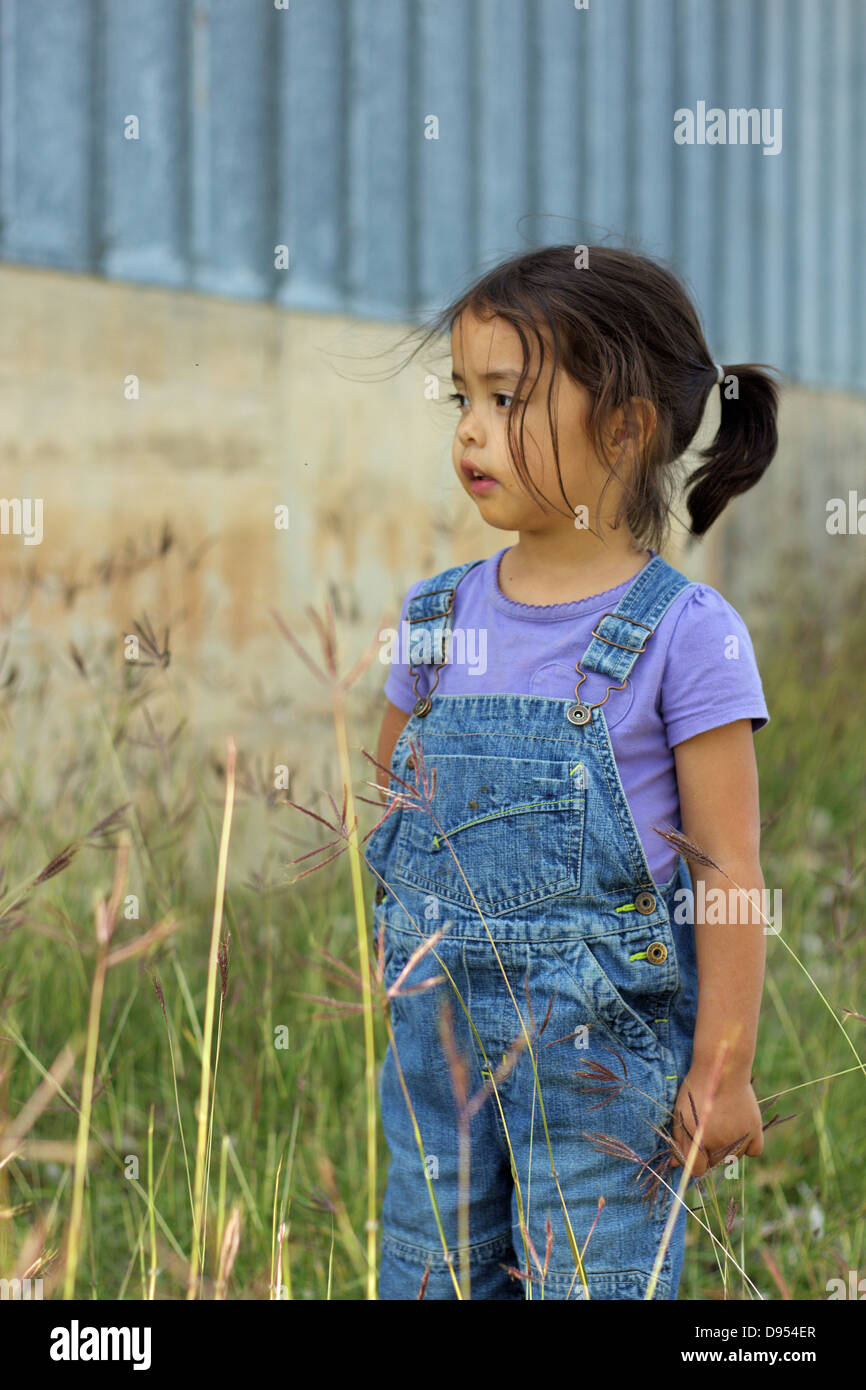 Little girl wearing overalls stands in field Stock Photo - Alamy