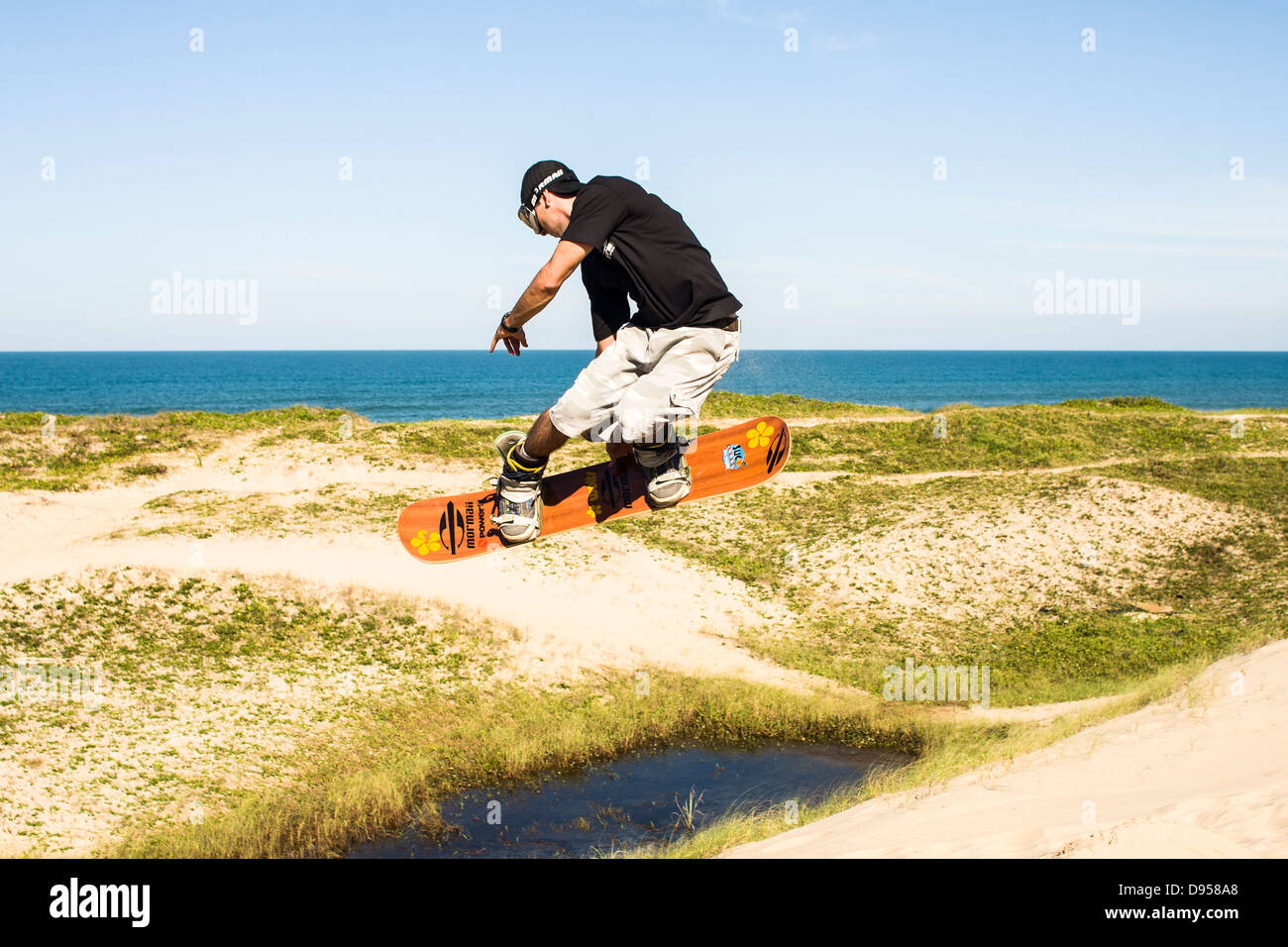 Sandboarder jumping and holding his board on the dunes of  Praia Grande. Stock Photo