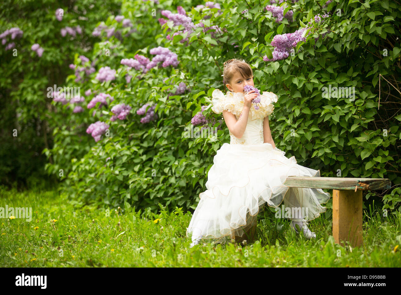 Little lovely girl with a bouquet of lilacs sitting on a bench in the ...