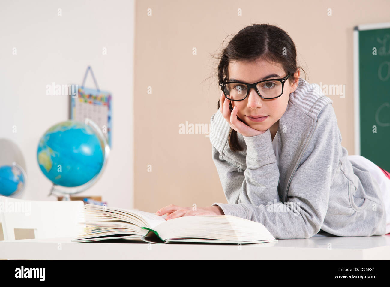 Girl Lying on Stomach Reading Book in Classroom, Mannheim, Baden-Wurttemberg, Germany Stock Photo
