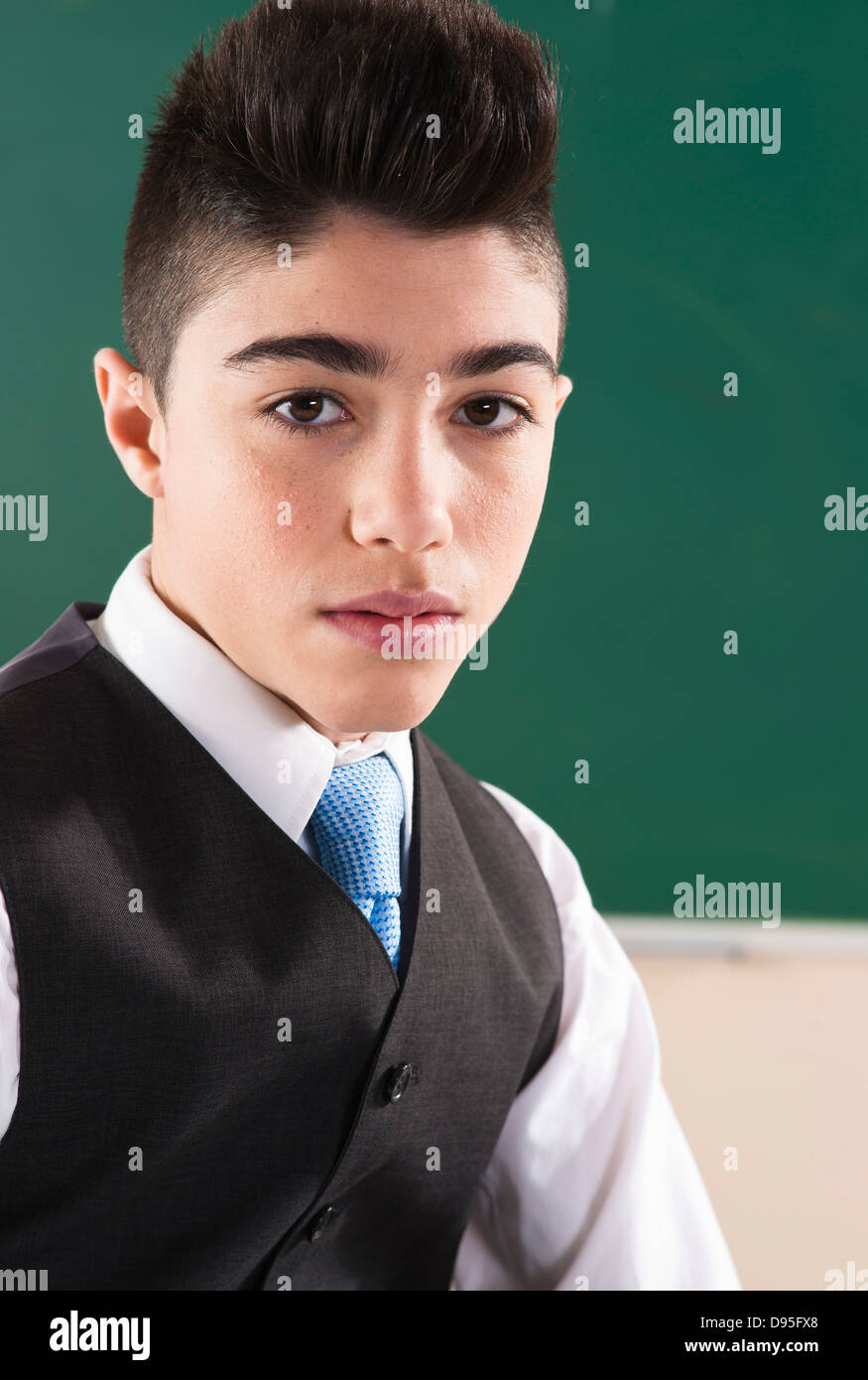 Head And Shoulders Portrait Of Boy In Front Of Chalkboard In Classroom