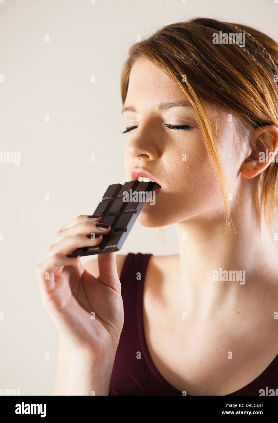 Teenage Girl Eating Chocolate with Eyes Closed, Studio Shot on White Background Stock Photo