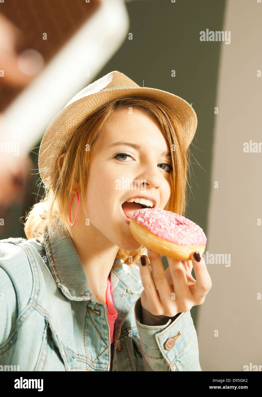 Head and shoulders portrait of teenage girl wearing hat and eating a