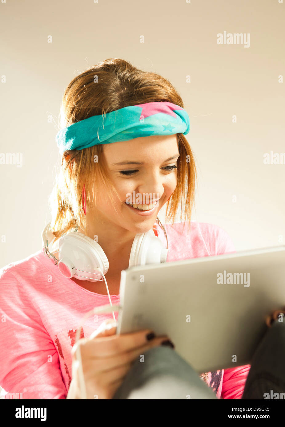 Head and shoulders portrait of teenage girl wearing a headband, headphones and using a tablet in studio. Stock Photo