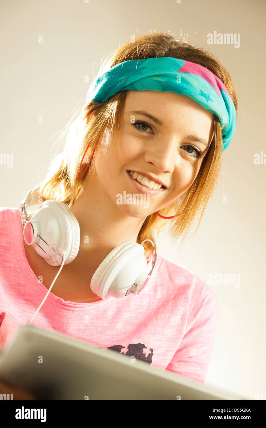 Head and shoulders portrait of teenage girl wearing a headband, headphones and using a tablet in studio. Stock Photo