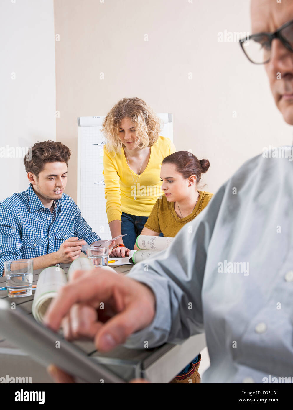 Close-up of Mature Businessman using Calculator with Young Colleagues Meeting in Background Stock Photo