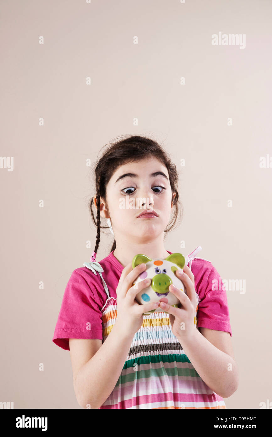 Portrait of Girl Looking Cross Eyed at Piggy Bank in Studio Stock Photo