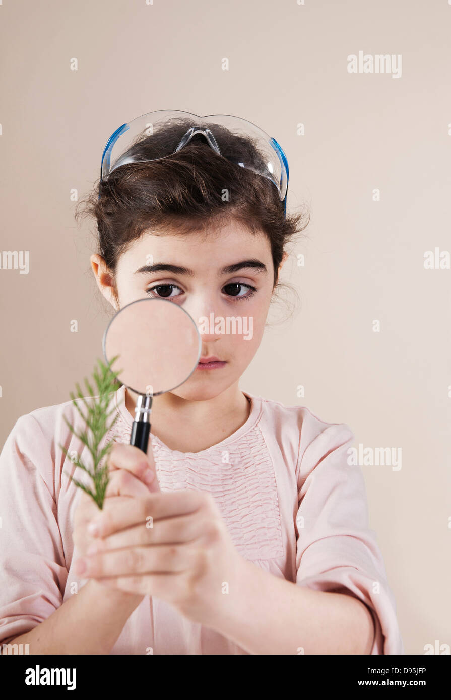 Portrait of Young Girl Wearing Goggles on Head and Looking through Magnifying Glass at Plant, Studio Shot Stock Photo