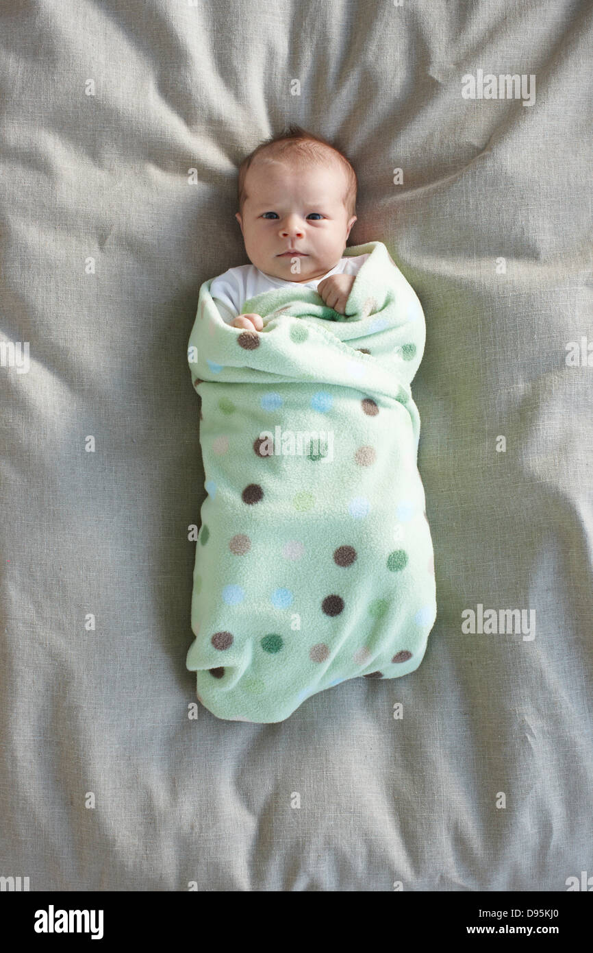 newborn baby girl in a white undershirt sleeping on a bed swadled in a