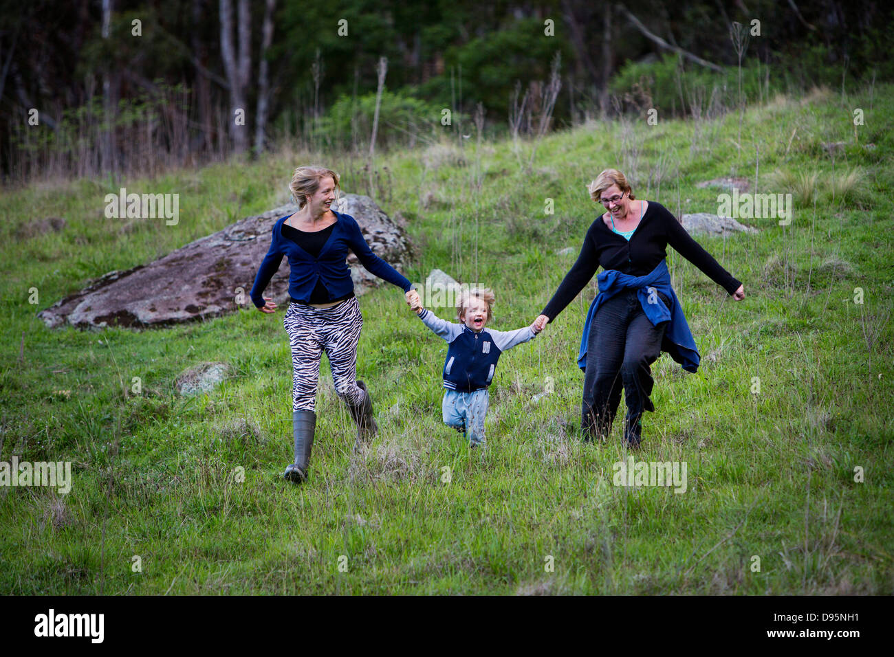 Family group of mother, daughter and grandson run down hill holding hands and laughing Stock Photo
