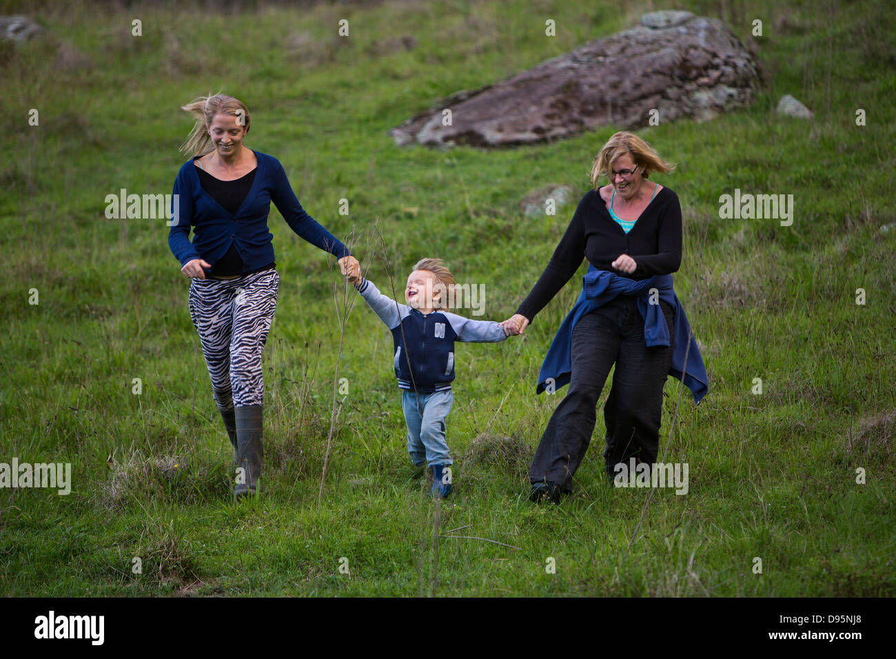 Family group of mother, daughter and grandson run down hill holding hands and laughing Stock Photo