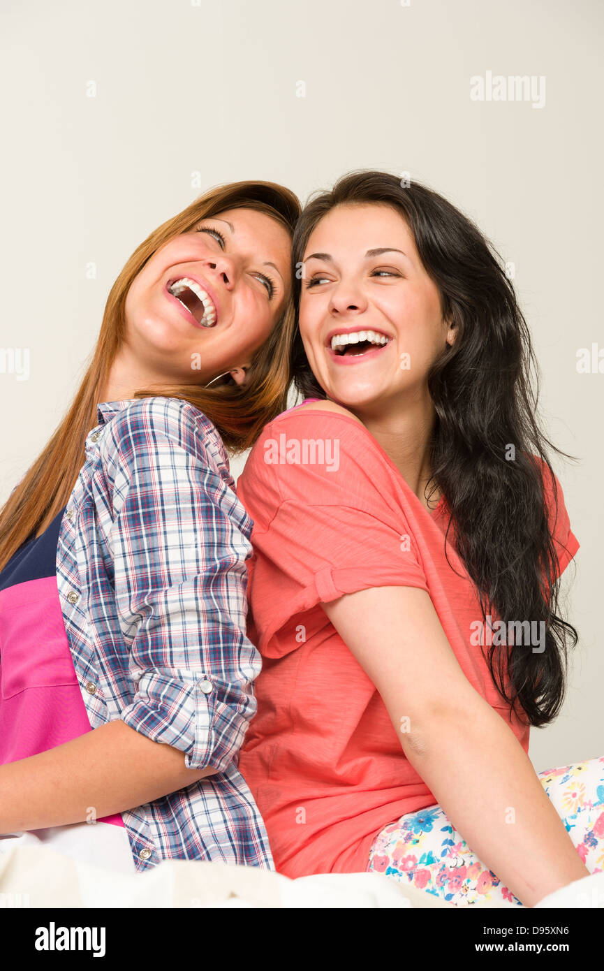 Playful sisters sitting back-to-back and laughing Stock Photo