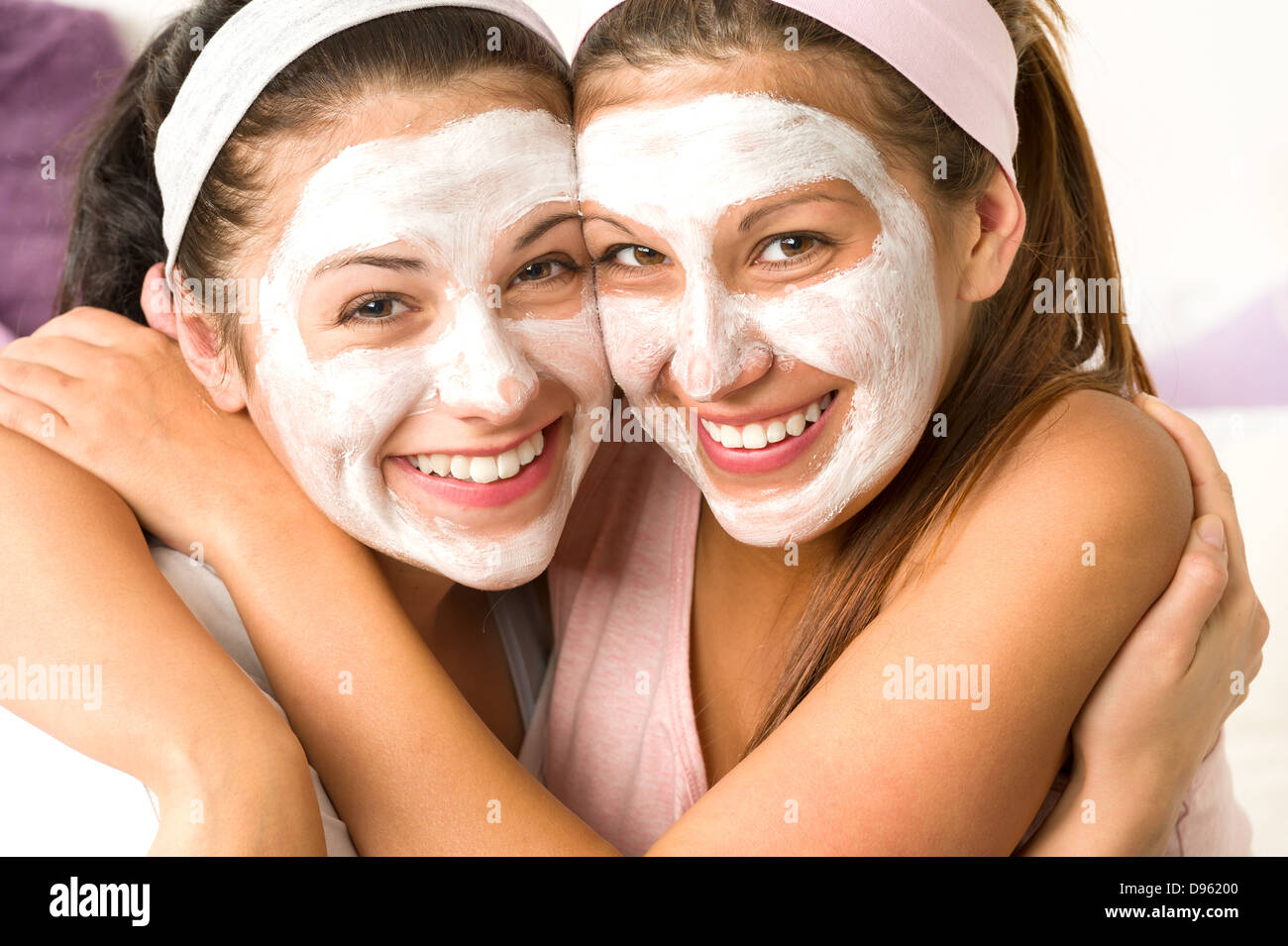 Blissful girls applying white facial mask hugging each other Stock Photo