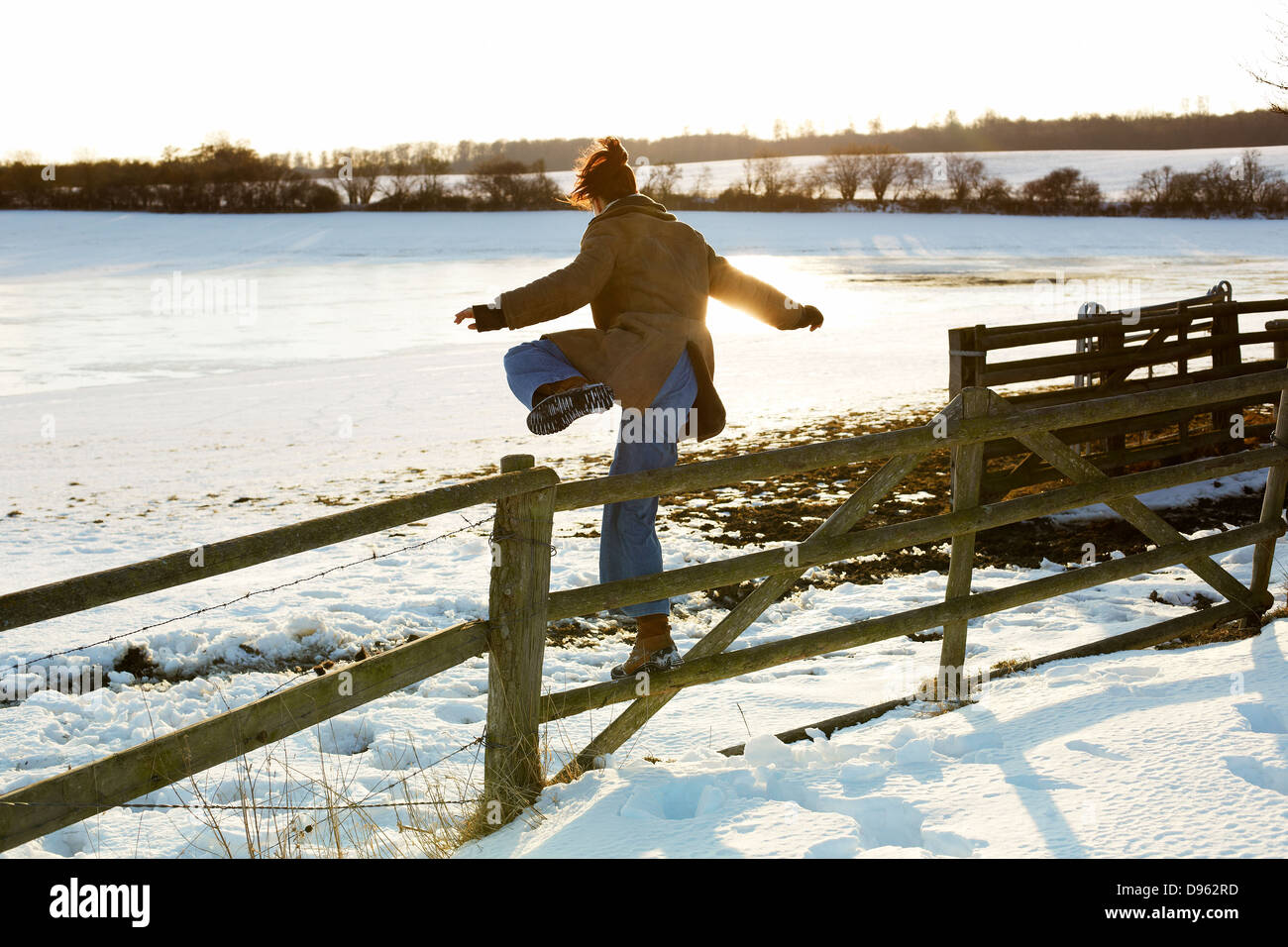 Germany, Mid adult woman jumping over cow fence Stock Photo