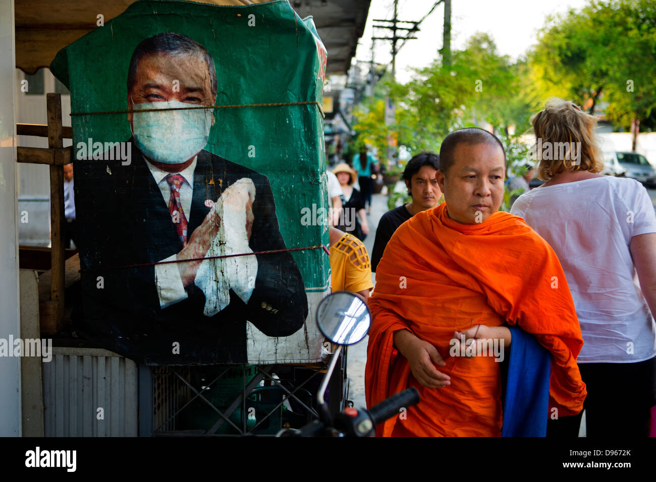 Buddhist monk passing street poster of man wearing hygiene mask Stock Photo