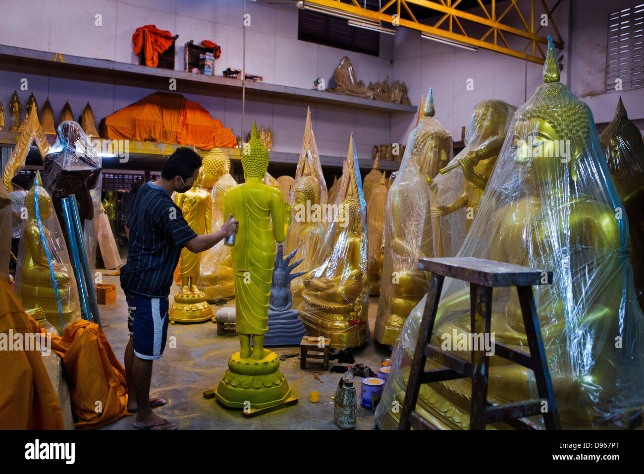 Workshop with man spraying Buddhist figures and statues, Bangkok, Thailand Stock Photo