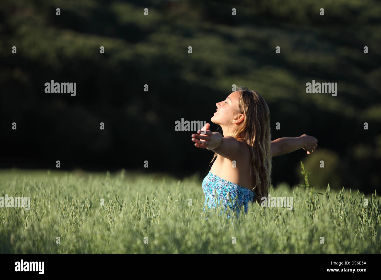 Attractive woman breathing joyful with raised arms in a green meadow with a dark background Stock Photo
