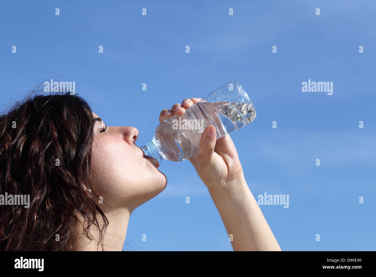 Profile of a beautiful woman drinking water from a plastic bottle with a blue sky in the background Stock Photo