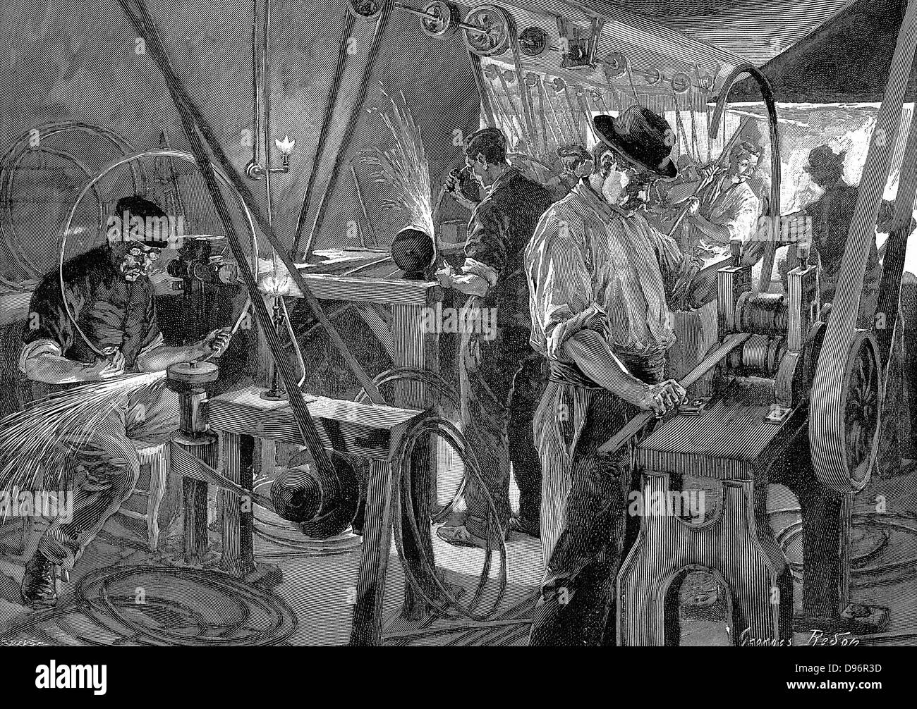 Bicycle Manufacture, France:  Shaping the wheel rims. Machinery all driven from central power source through belt-and-shafting. In right foreground man is passing metal strip through shaping machine, it is then passed along production line to forge at rear.  Men at grindstones wear protective goggles. Fish-tail gas lights provide illumination.  Wood engraving Paris, 1896. Stock Photo