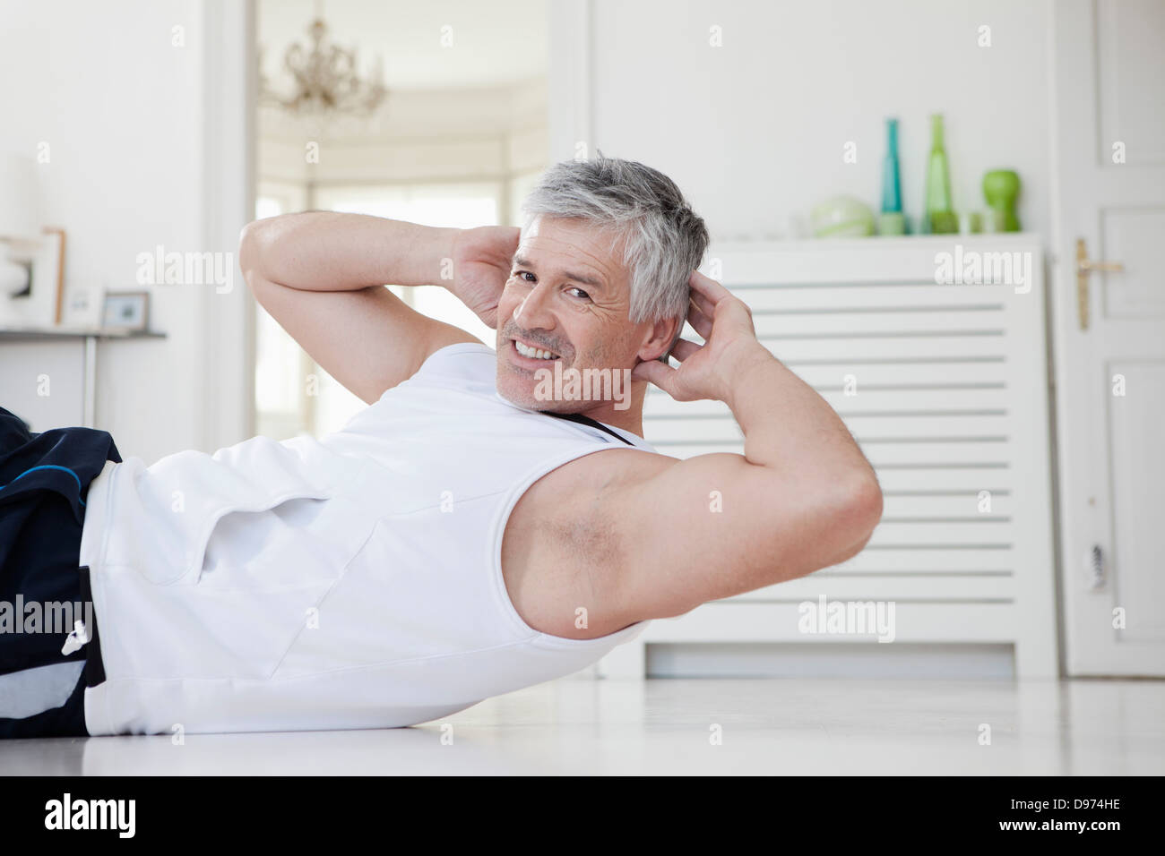 Germany, Bavaria, Munich, Mature man doing sit-ups at home, smiling Stock Photo