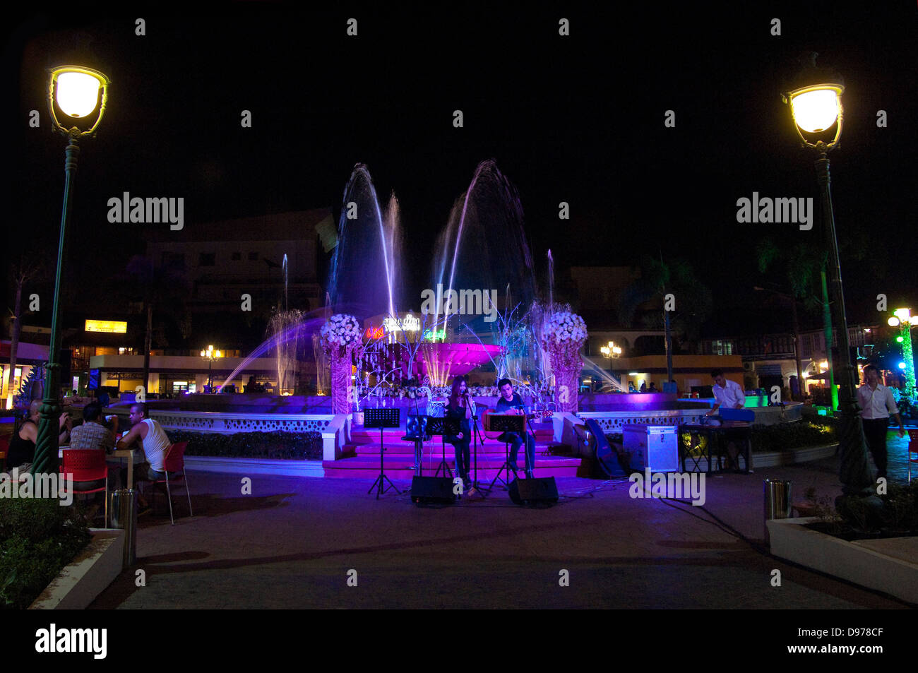 Horizontal view of a duet performing infront of the illuminated Nam Phou fountain in Vientiane at night. Stock Photo