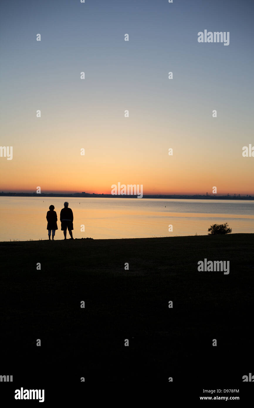 An elderly couple watch a sun set over a still bay in Dublin city, Ireland. Stock Photo