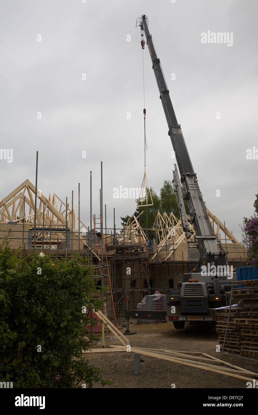 Crane lifting timber roof frame into place on building site, UK Stock Photo