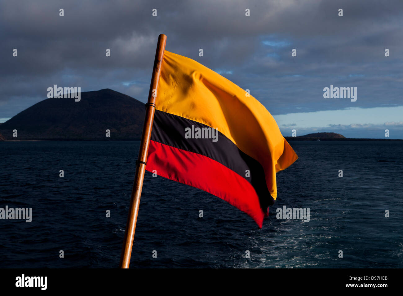 The Ecuadorian flag fills the foreground when looking back from the Grand Odyssey yacht towards James Island, the Galapagos. Stock Photo