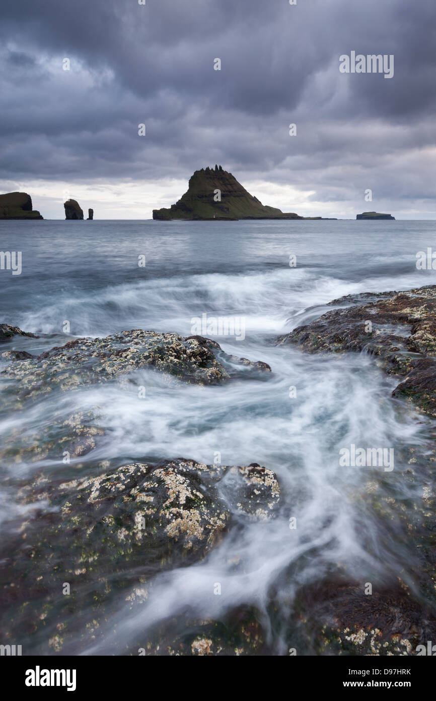 Waves swirl around the rocky seashore of Vagar, looking towards the beautiful island of Tindholmur in the Faroe Islands. Stock Photo