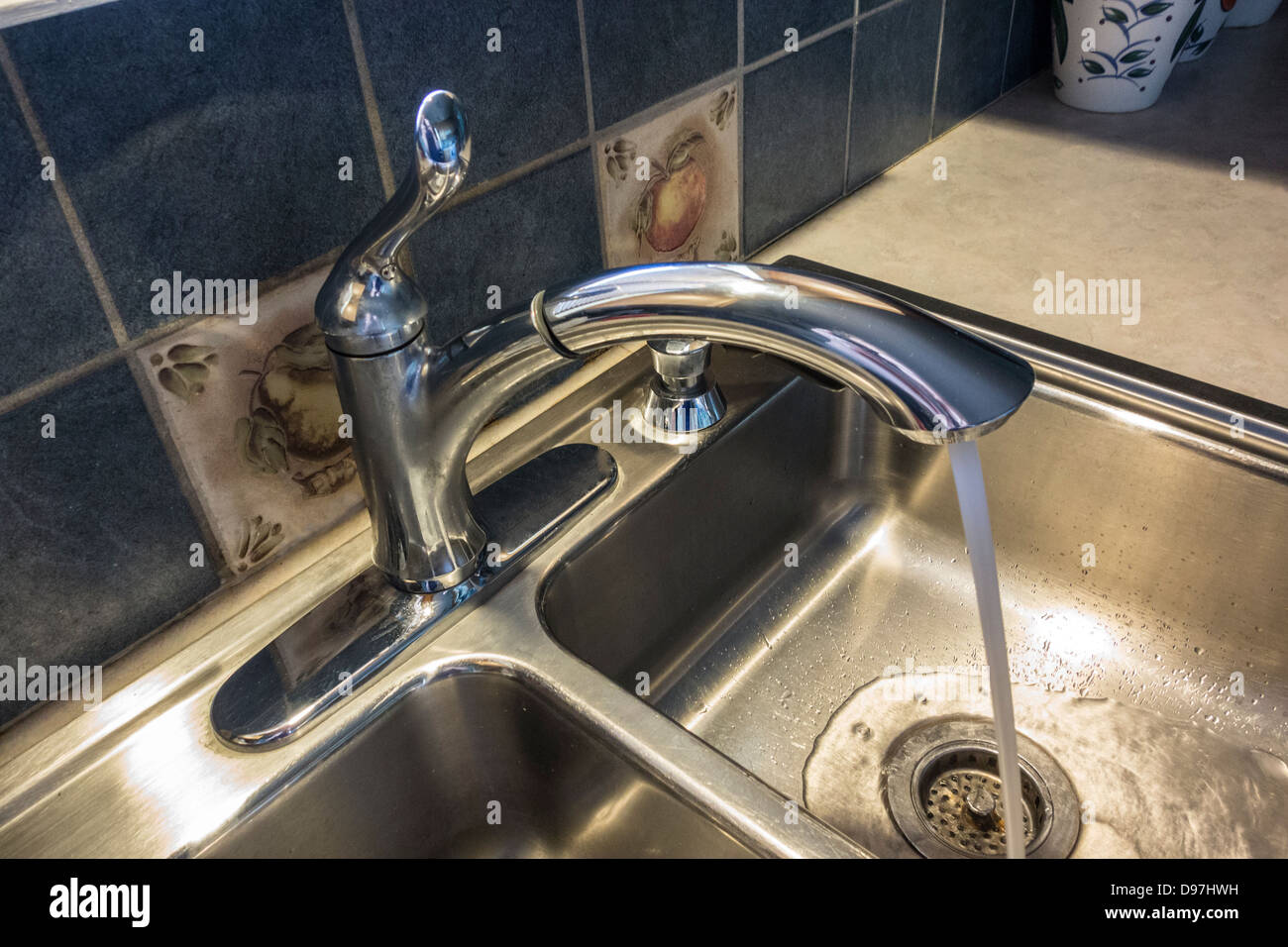 Kitchen faucet with running water into stainless steel double sinks. Closeup. USA. Stock Photo