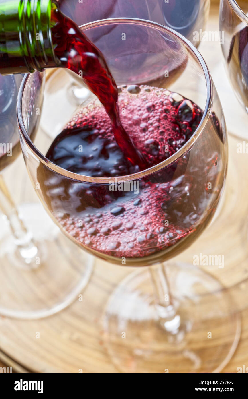 Red wine being poured into a glass, one of several on a tray. Stock Photo