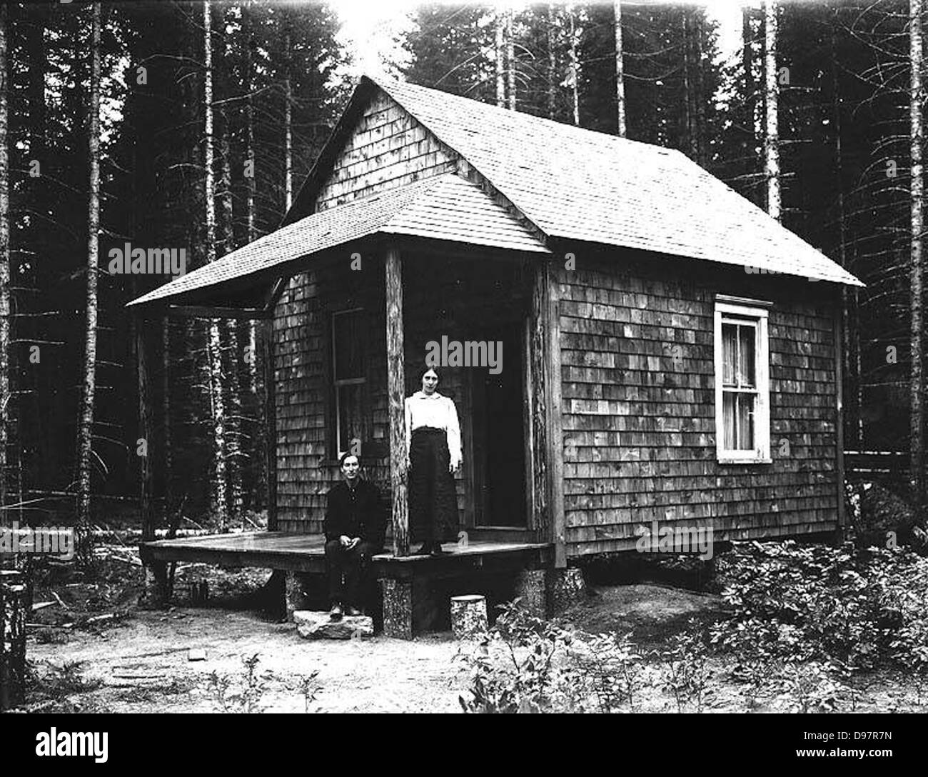 Ortie Bowen and wife on the porch of a cabin in forest setting, Washington State Stock Photo