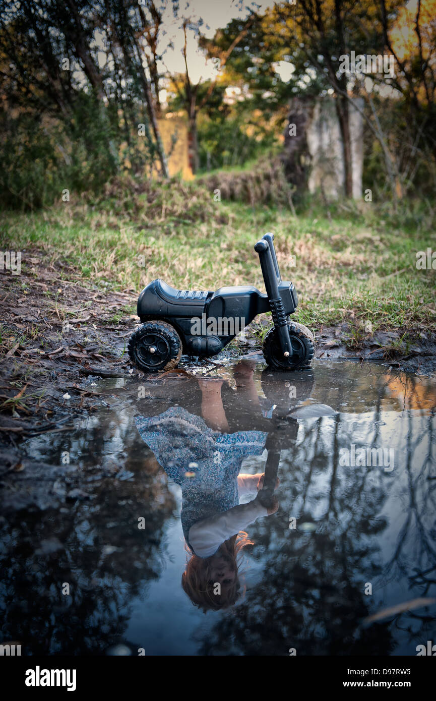 Small black plastic toddler scooter standing next to a puddle with only the toddlers reflection in water. Stop Child abuse. Love Stock Photo