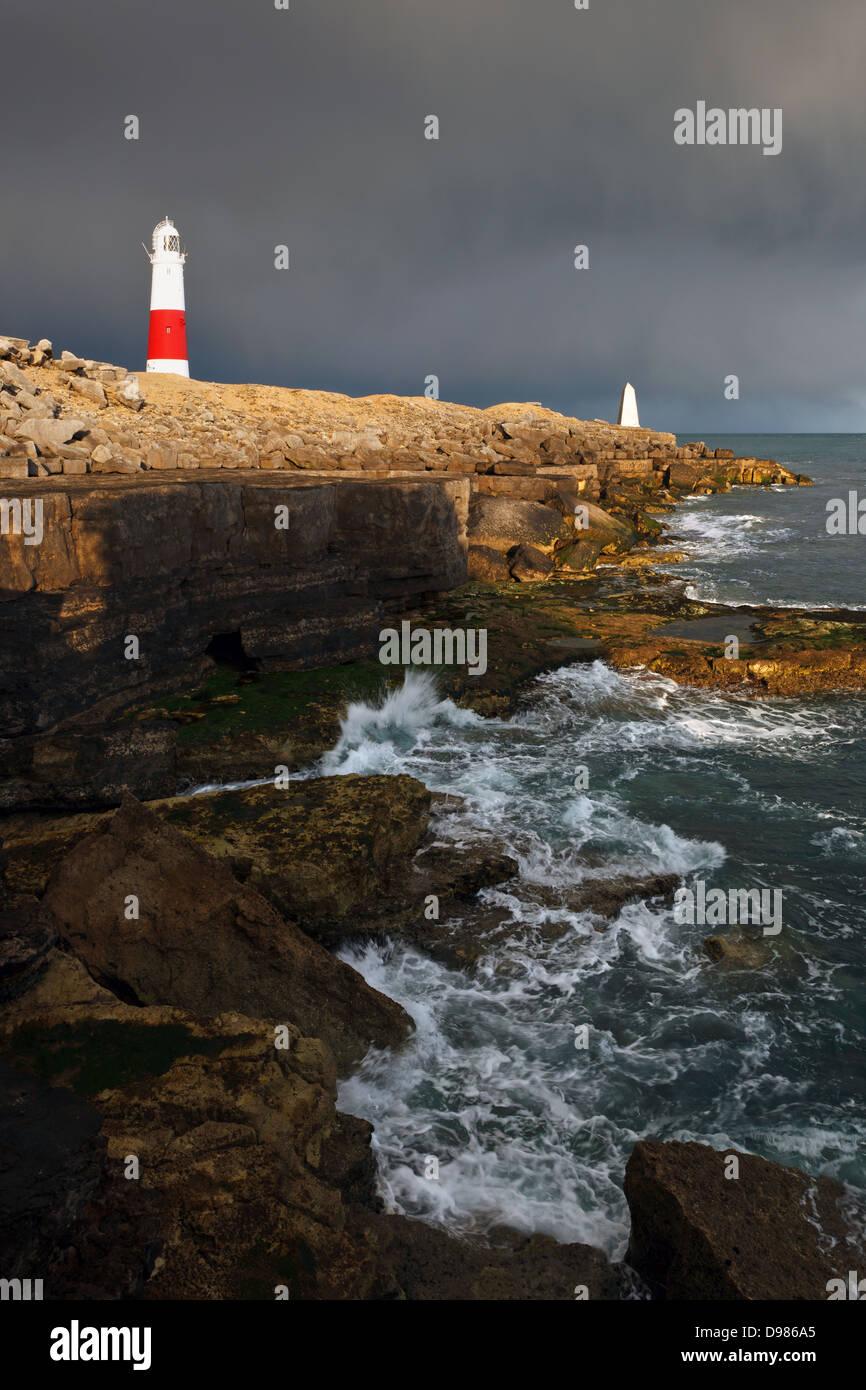 Portland Bill lighthouse in Dorset with the setting sun lighting up the buildings against the incoming dark storm clouds. Stock Photo