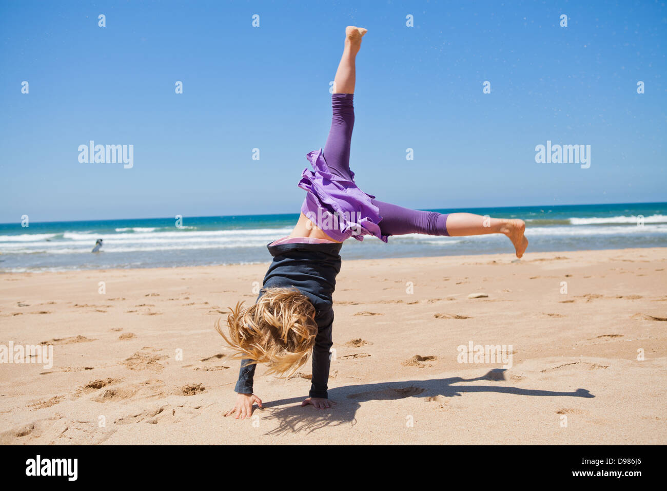 Cute young girl doing cartwheel in sand at beach with blue sky and