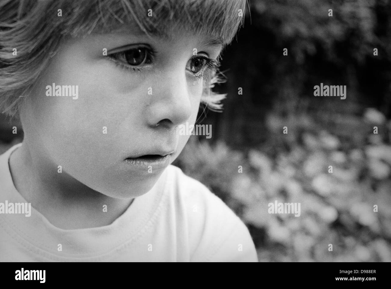 A 4 year-old girl sheds a tear during an emotional moment while playing in her back garden. Seen in close-up detail we see a tear creeping down her right eye and another making its way down her left cheek - her large eyes looking sad and upset. Stock Photo