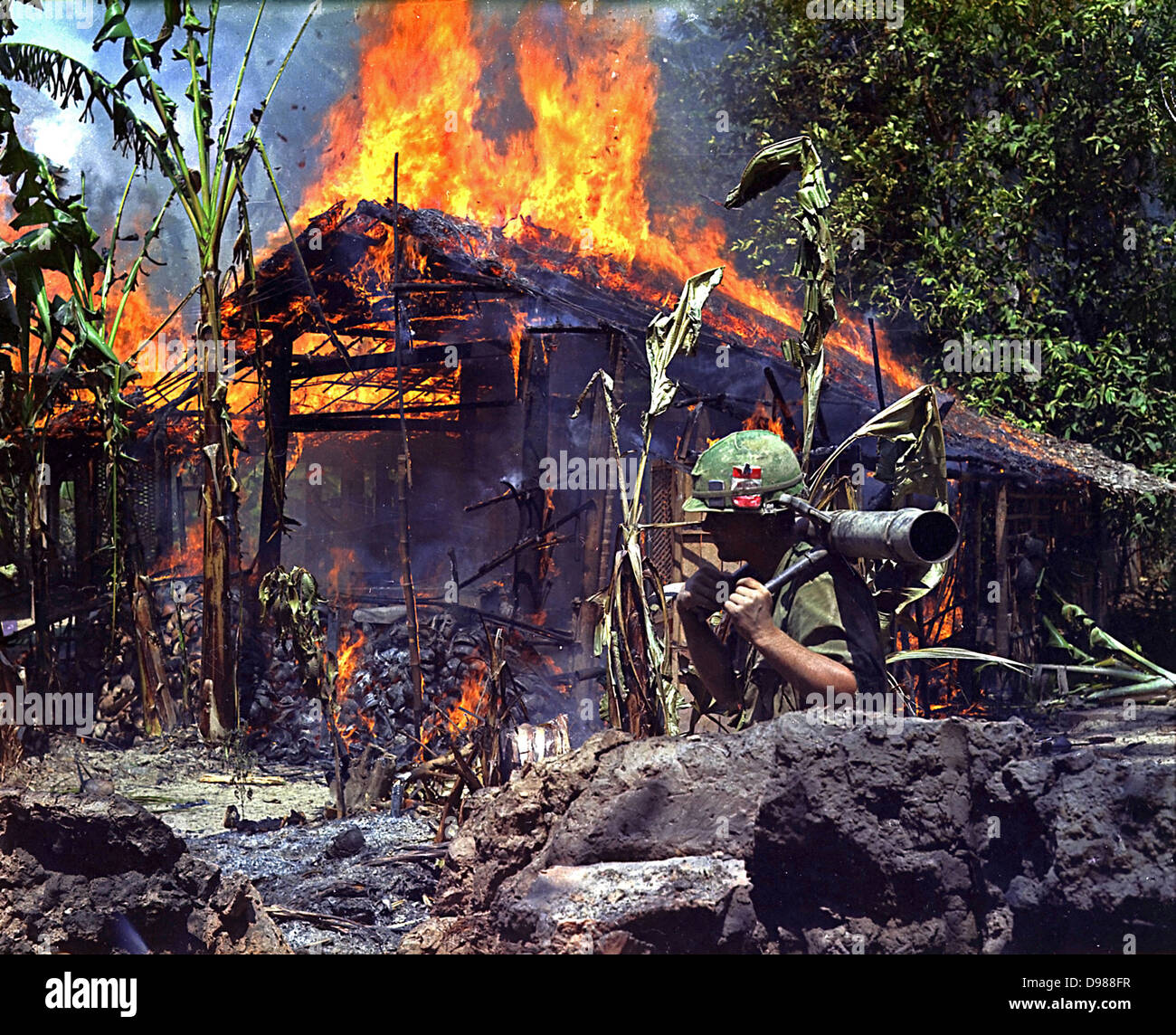 My Tho, Vietnam. A Burning Vietcong Base Camp. In the foreground is Private First Class Raymond Rumpa, St Paul, Minnesota, C Company, 3rd Battalion, 47th Infantry, 9th Infantry Division, with 45 pound 90mm recoiless rifle, 4 May 1968. Stock Photo