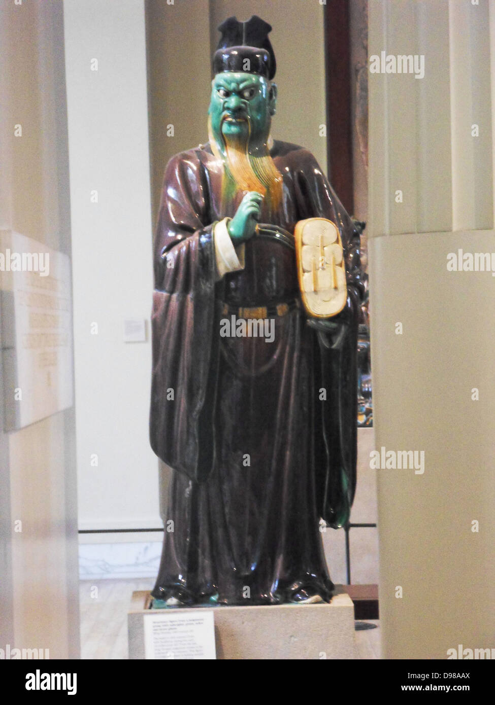 Stoneware figure from a judgement group with aubergine, green, ochre and straw glazes.  Ming Dynasty, 16th century AD.  The belief in Hell entered China with Buddhism during the early 1st millennium AD.  From the late Tang Dynasty judgement scenes in the underworld were common.  This figure of a judge's assistant is holding records of evil deeds under his left arm. Stock Photo