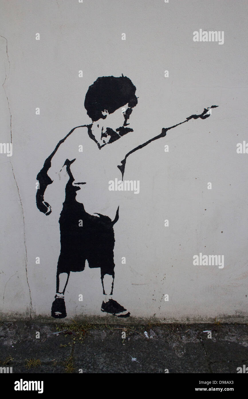 A spray painted boy pointing into the distance, in black on a grey background in the style of Banksy. Stock Photo