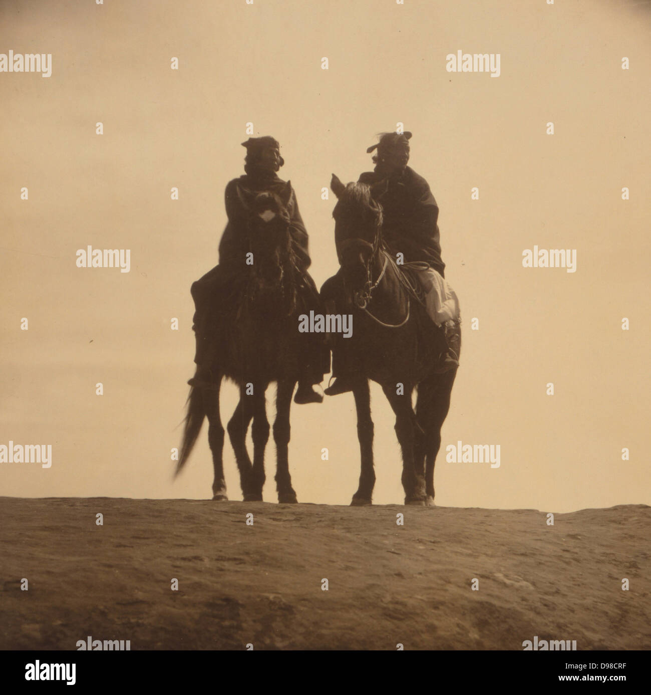Two native American men mounted on horses, in silhouette, gazing off into the distance, c1904. Photograph by Edward Curtis (1868-1952 ). Stock Photo