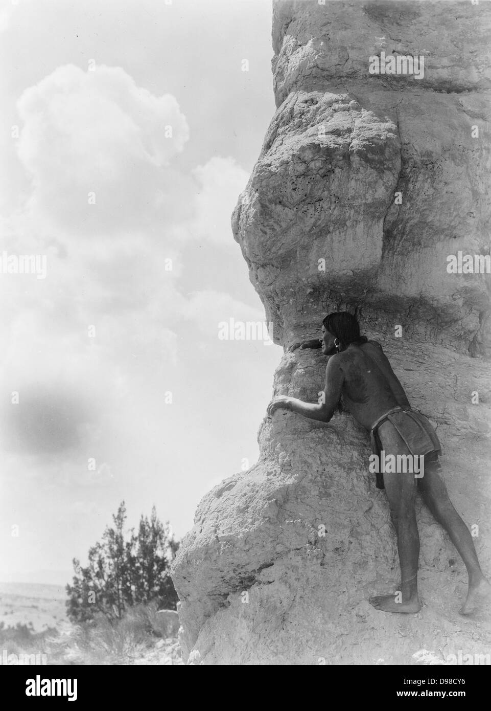 San Ildefonso man peering from behind large rock formation, c1927. Photograph by Edward Curtis (1868-1952). Stock Photo