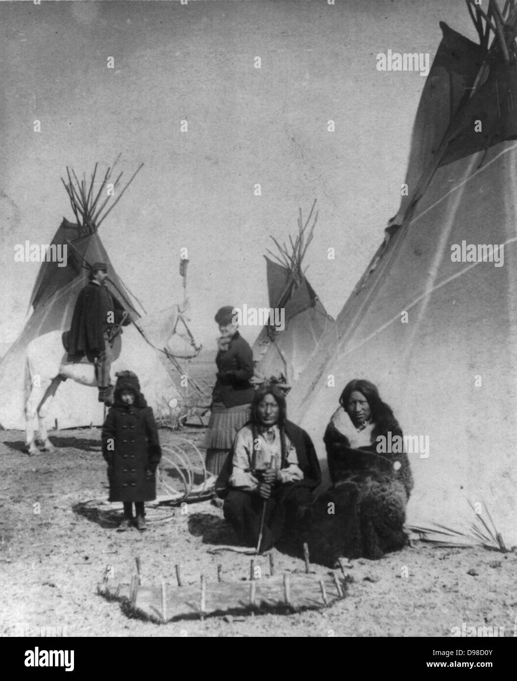 Commanding Officer inspecting the Sioux Indian Camp, also the Mediciine Tepee and flag of red flannel, with One Bull and Black Praire Chicken watching a hide that has just been stretched by squaws, 1882. Stock Photo